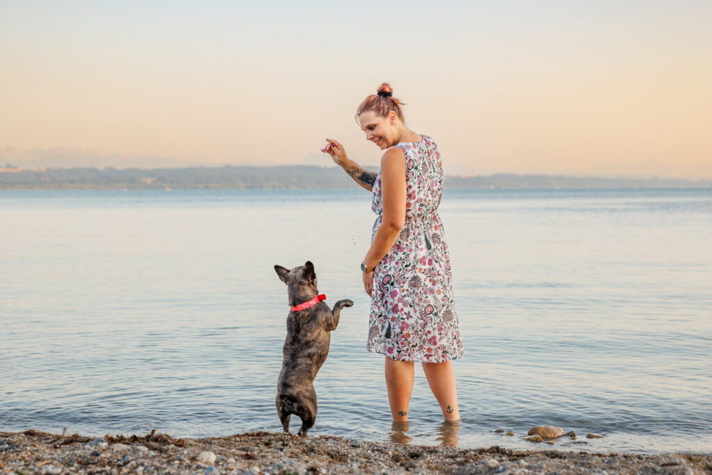 Une femme jouant avec son animale au bord de l'eau, heureux grâce à l'offre de communication animale et shooting photo de Sofia Rothen et Lakshmi Vibrations